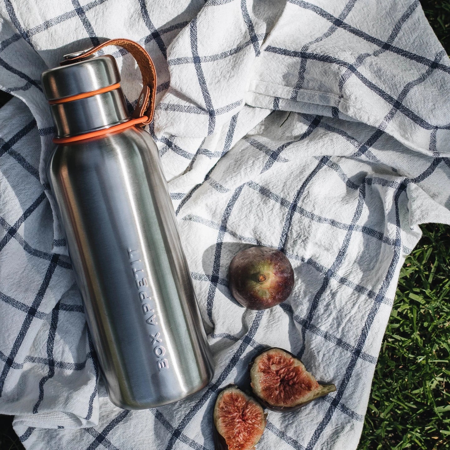 Insulated stainless steel water bottle with vegan leather accent. Shown at picnic with figs