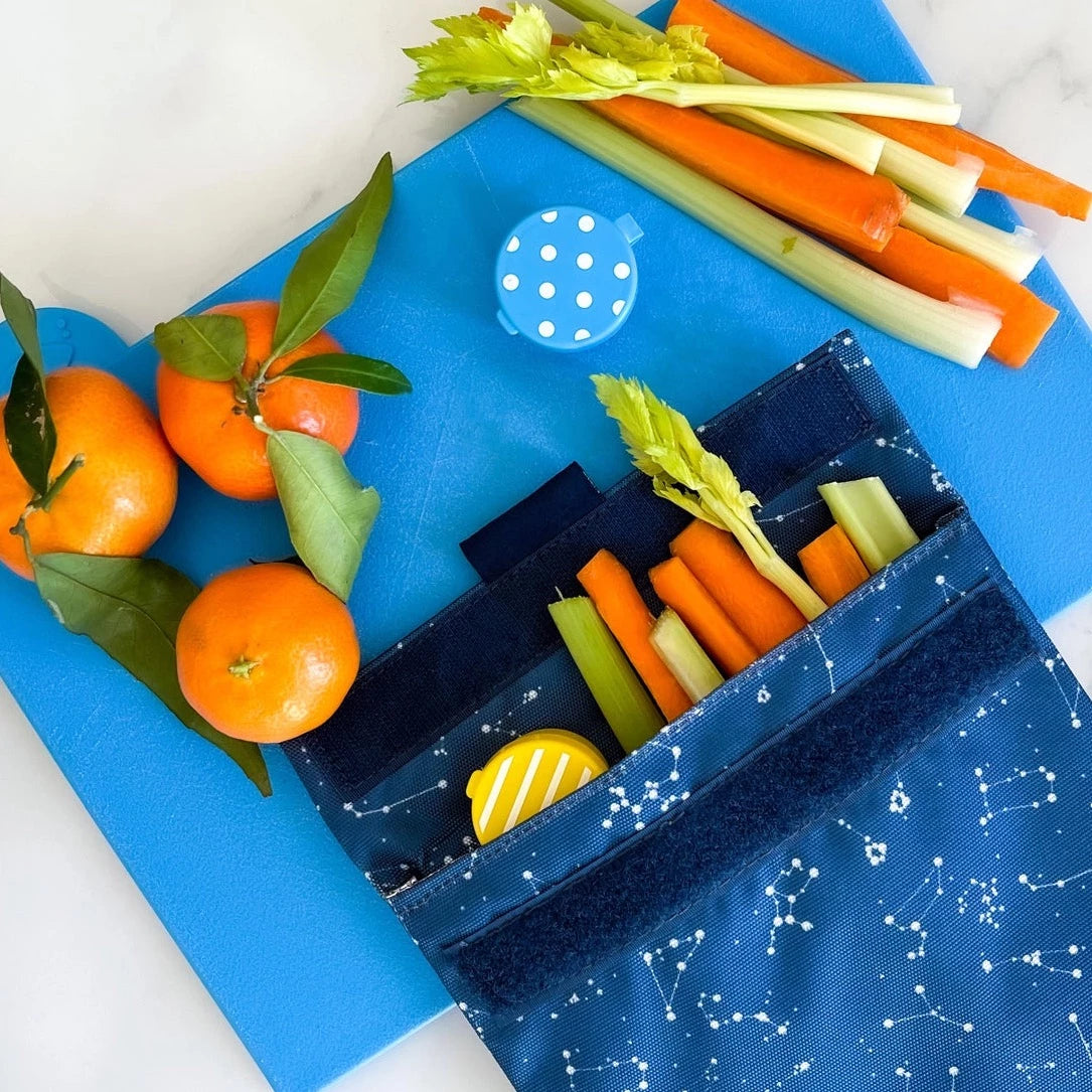 Reusable sandwich and snack bag, shown with veggies and fruits.  velcro closure and insulated interior.  Durable material.  white constellations on blue background.  wipe clean or throw in washing machine.