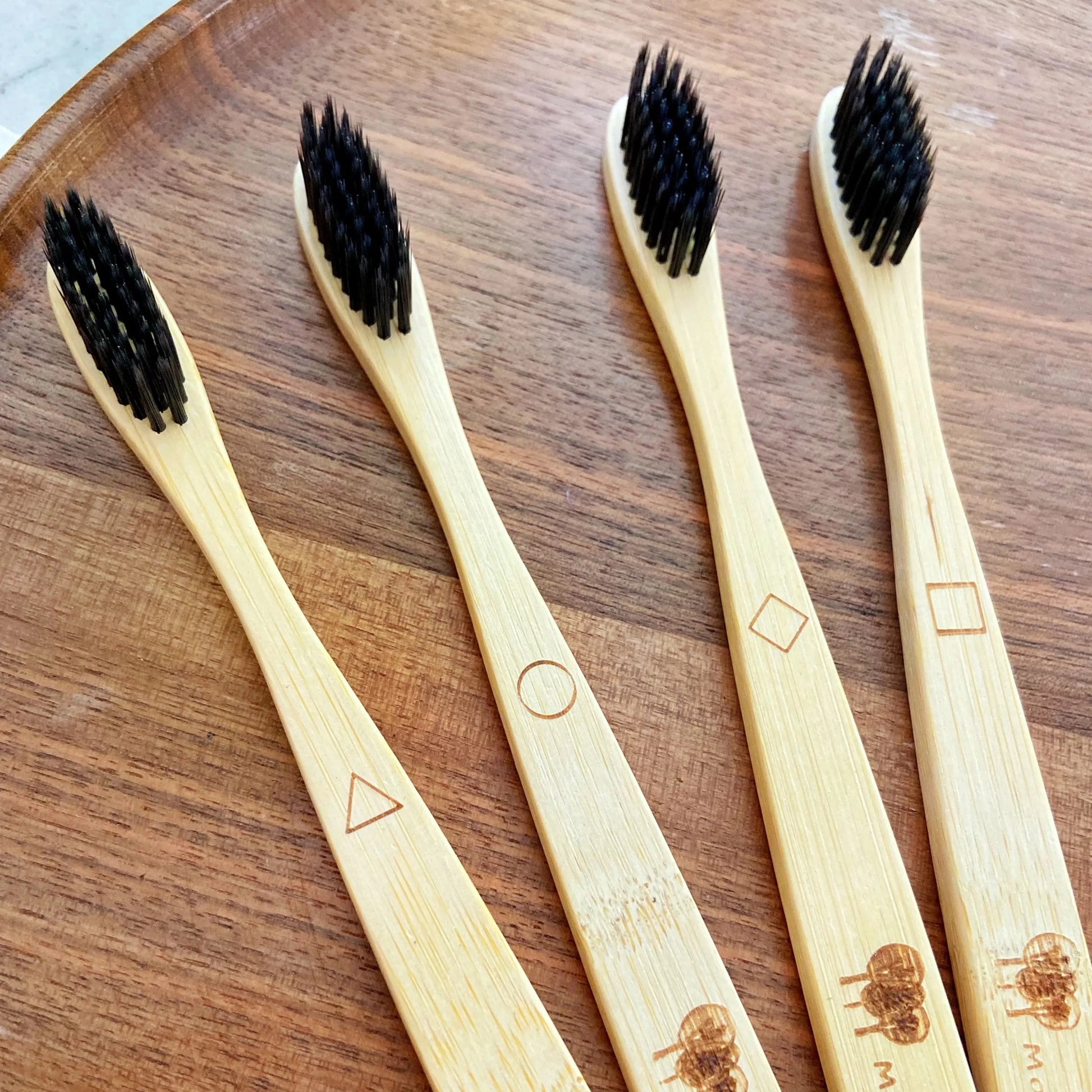 bamboo tooth brushes with active carbon bristles extra soft.  geometric shapes to tell them apart.  Up Close displayed on walnut tray