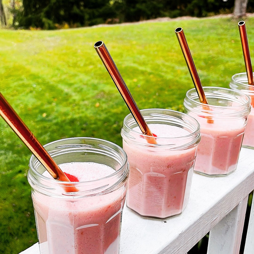 Rose Gold finish straws in raspberry smoothies. Glass Jars on white banister grass background