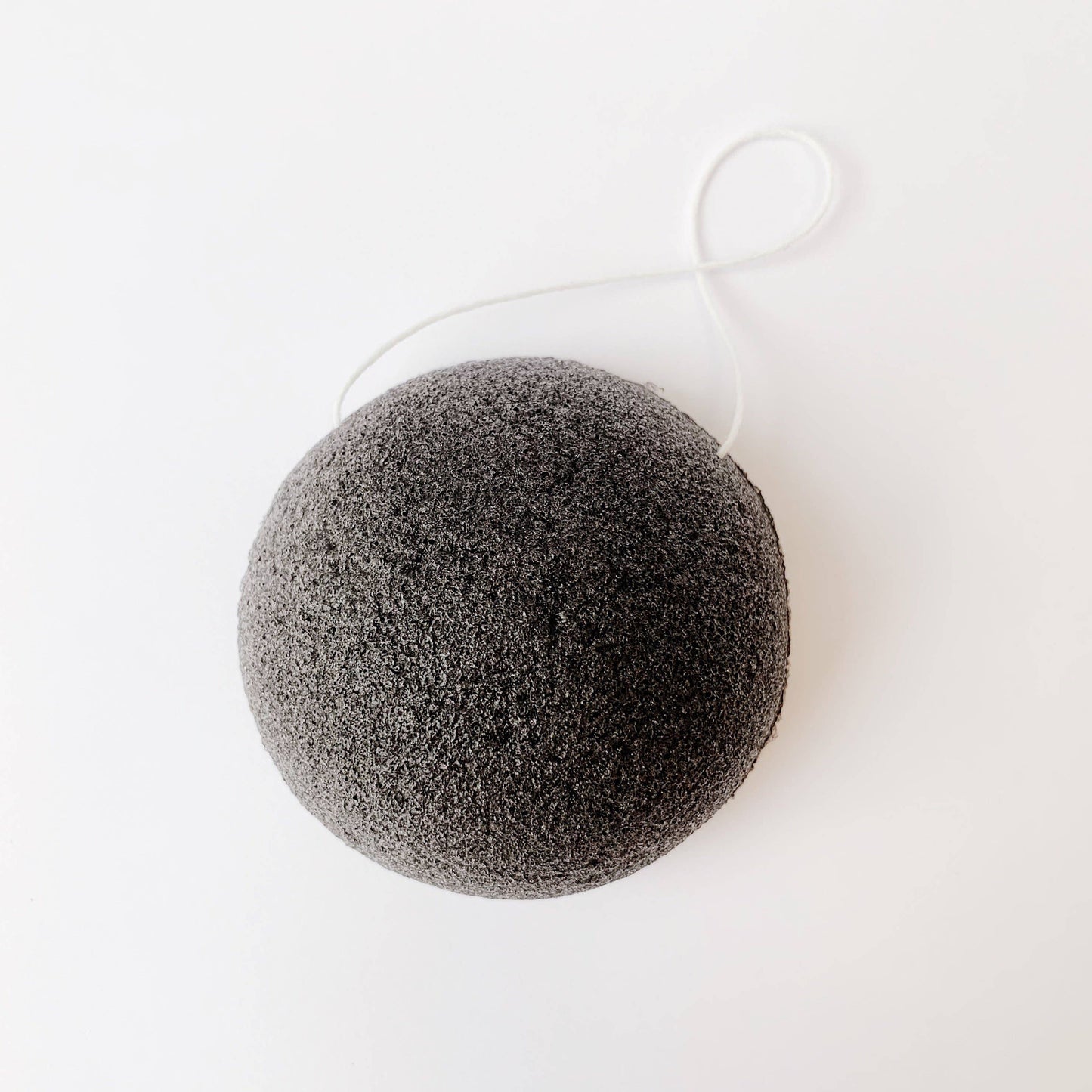 Top view. black konjac sponge with hanging string.  exfoliate gently.  conjac plant and carbon