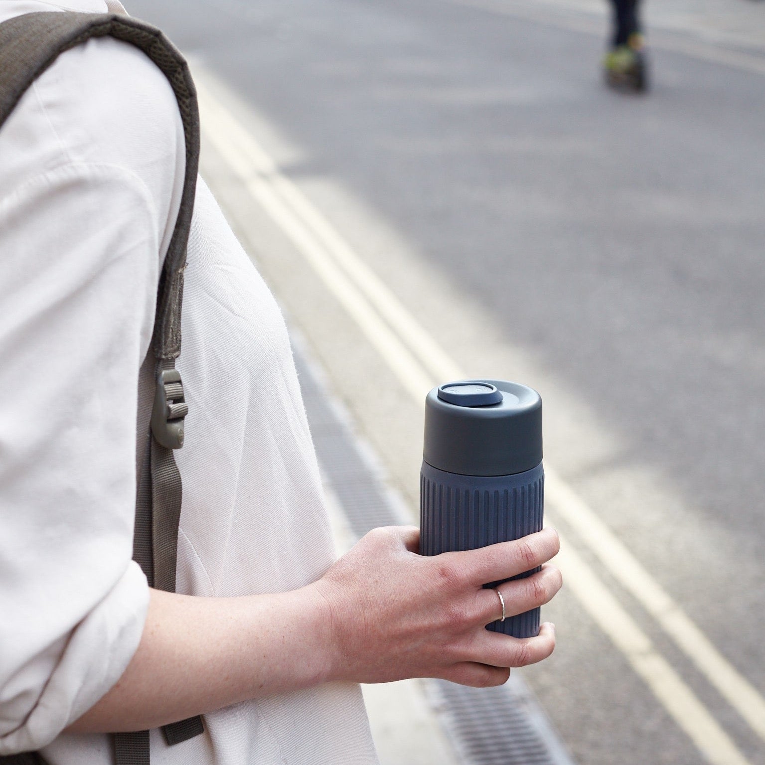 Woman holding slate colored glass travel cup in the street