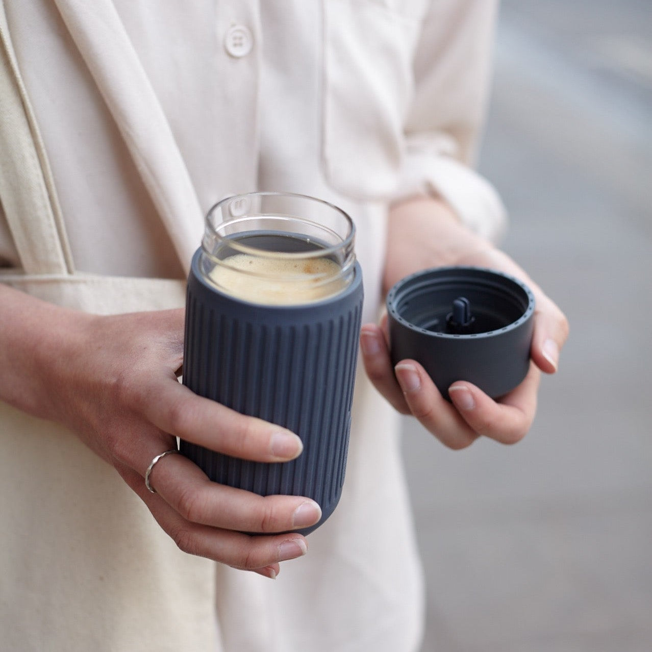 Woman holding open cup with beverage in it.  Glass travel cup, 100% leak proof.  State silicone wrap.  attractive design