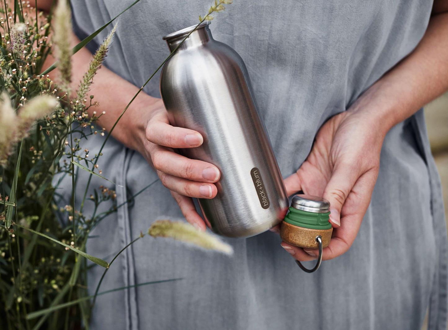 Woman holding open water bottle.  stainless steel single wall and cork lid with olive accent.  