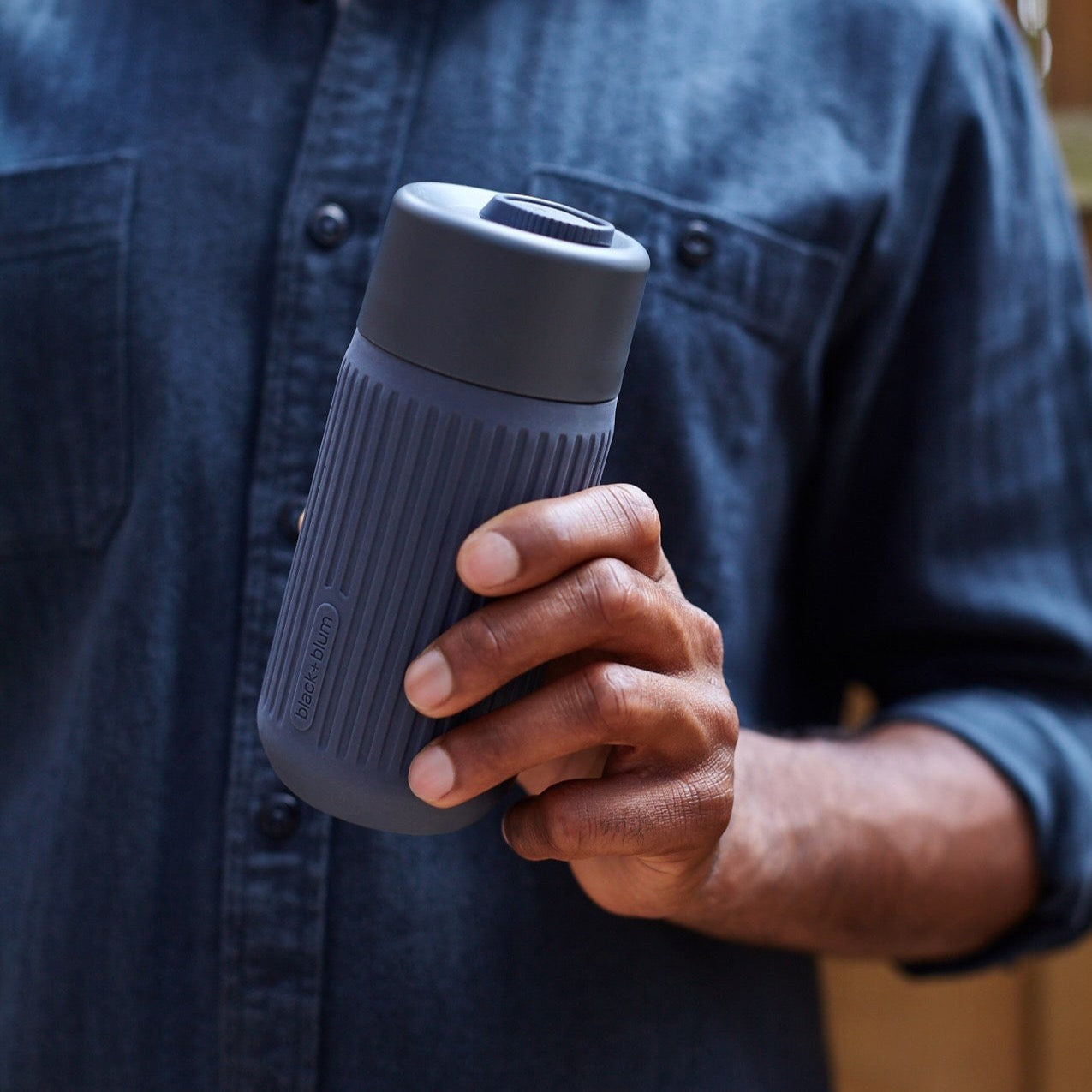 man holding slate colored glass travel cup